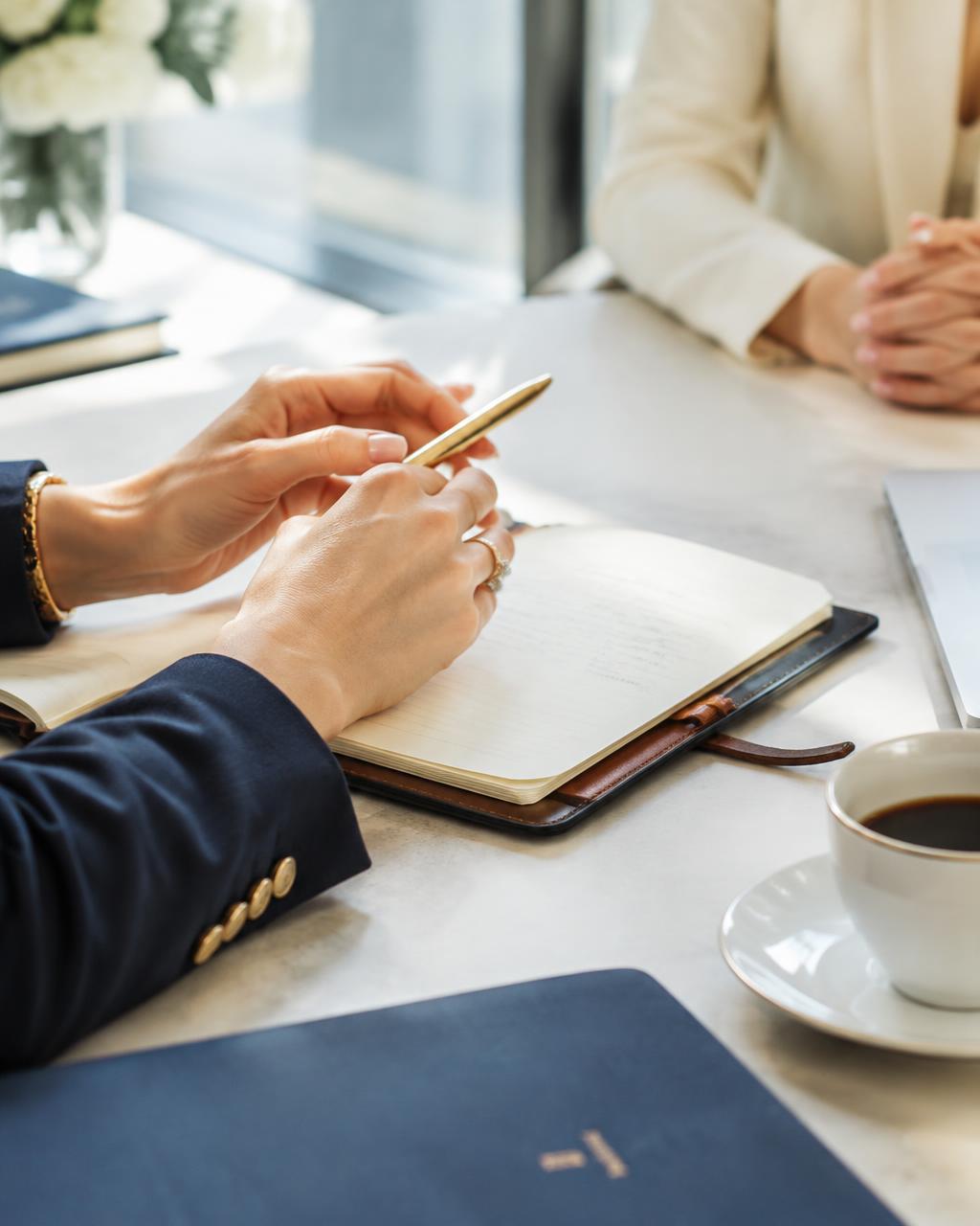 Hands with a gold pen over an open notebook during a coaching session